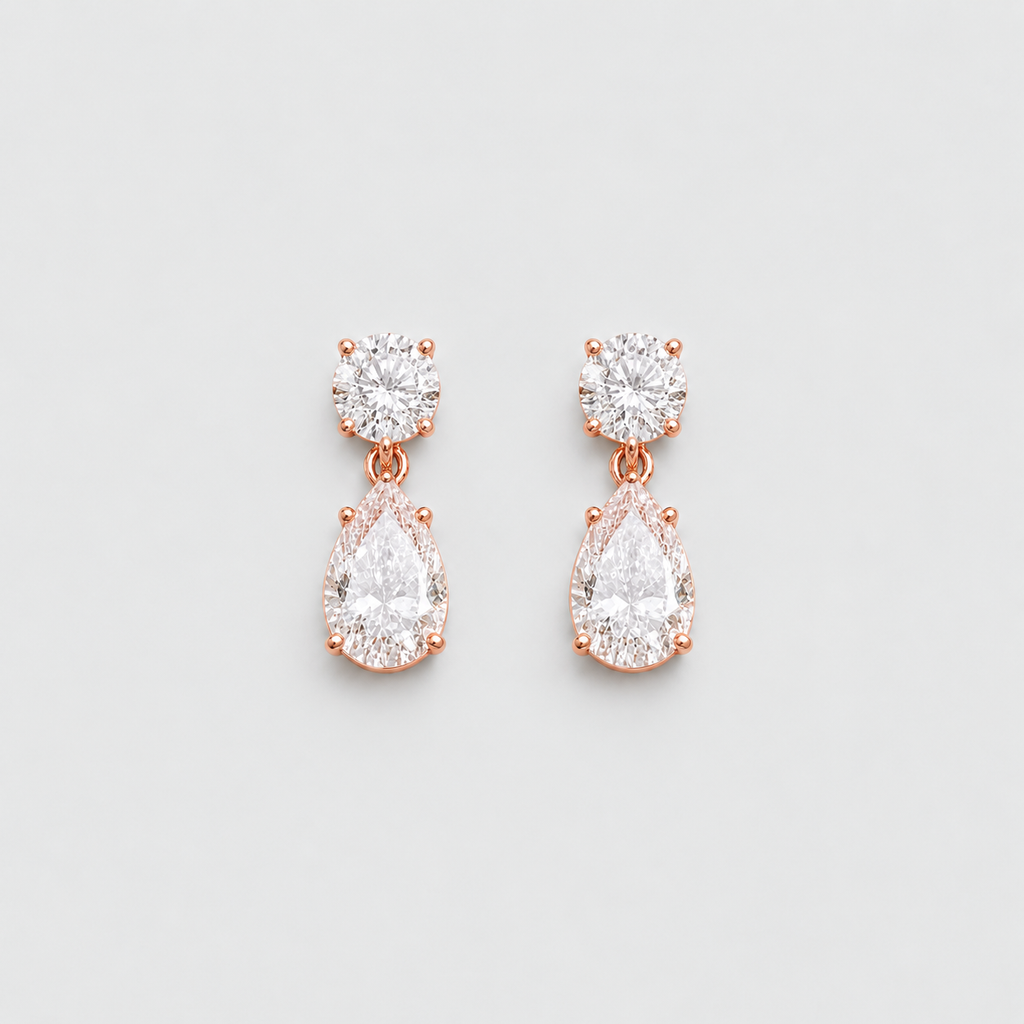 A pair of rose gold drop earrings with round and pear-cut clear gemstones, displayed on a clean light gray background.