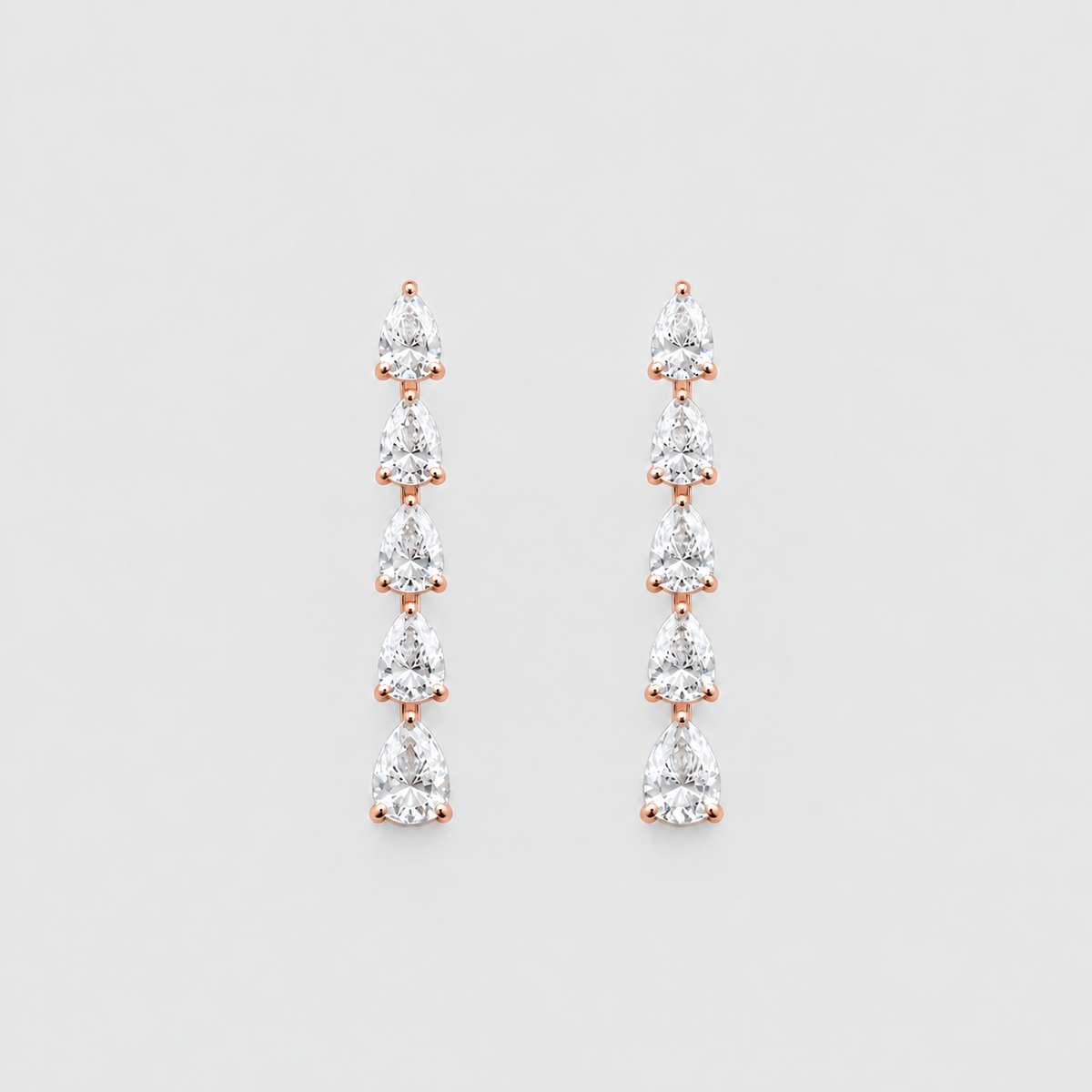 A pair of rose gold drop earrings featuring a vertical arrangement of seven pear-cut clear gemstones in a prong setting, displayed against a light gray background.