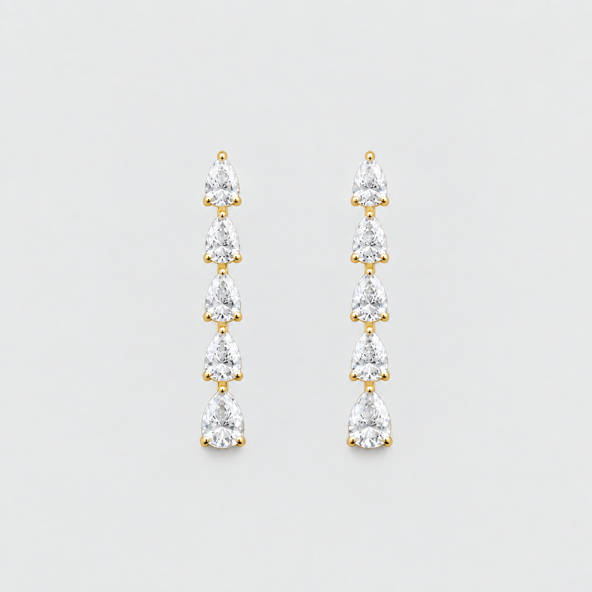 A pair of gold drop earrings featuring five pear-cut clear gemstones in a vertical dangle design, set against a solid light gray background.