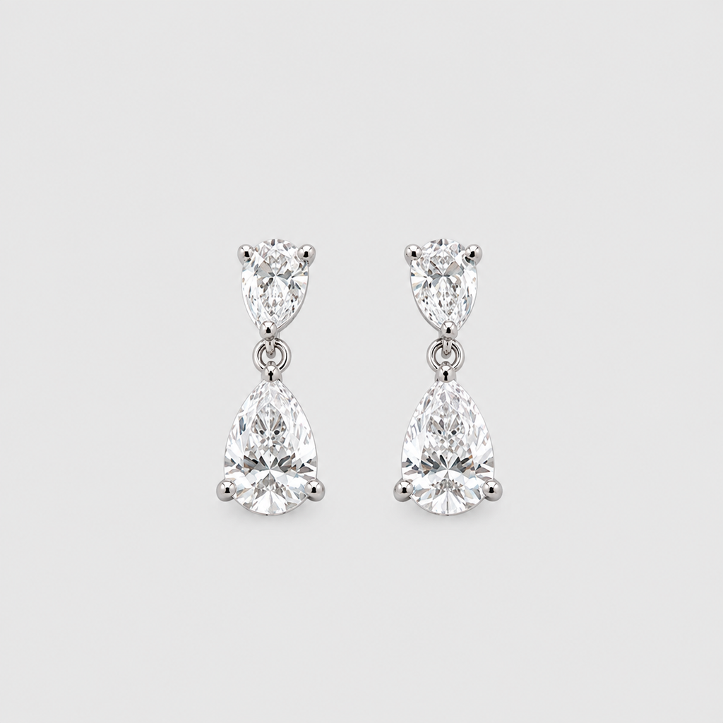 A pair of silver drop earrings featuring pear-cut clear gemstones in a three-prong setting, displayed against a light gray background.
