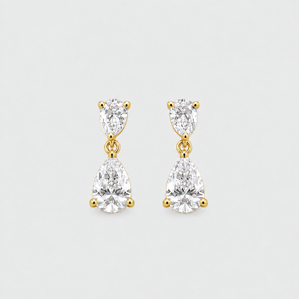 A pair of gold drop earrings featuring marquise-cut and pear-cut clear gemstones in prong settings, displayed on a light gray background.