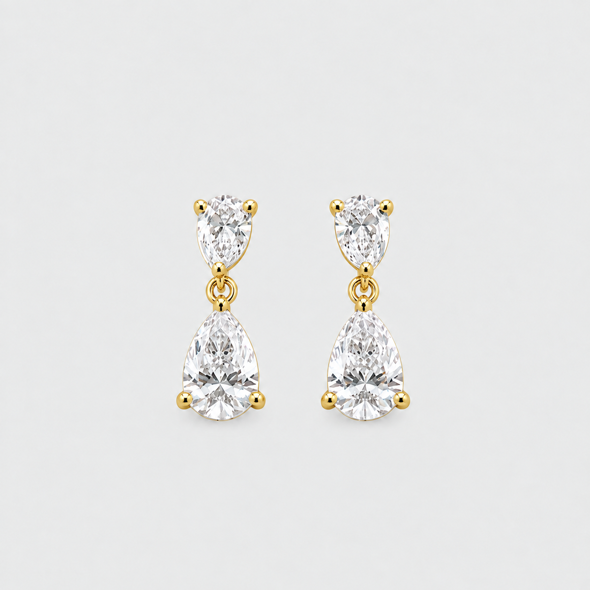 A pair of gold drop earrings featuring marquise-cut and pear-cut clear gemstones in prong settings, displayed on a light gray background.