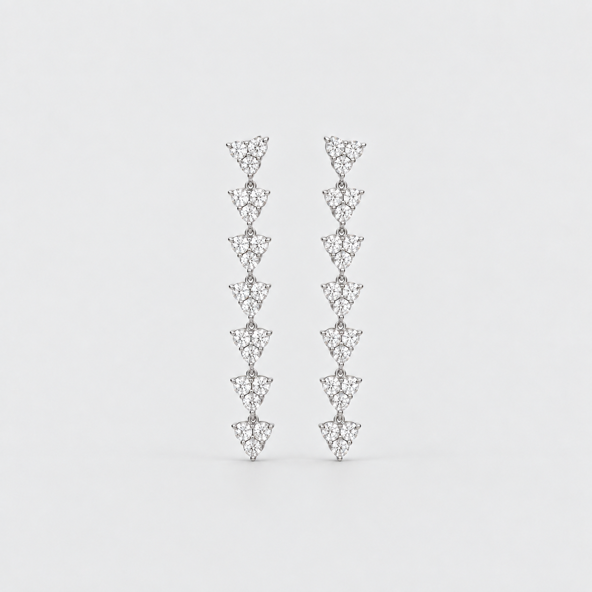 A pair of silver-toned drop earrings featuring a vertical stack of small triangular pavé diamond clusters, set against a plain light gray background.