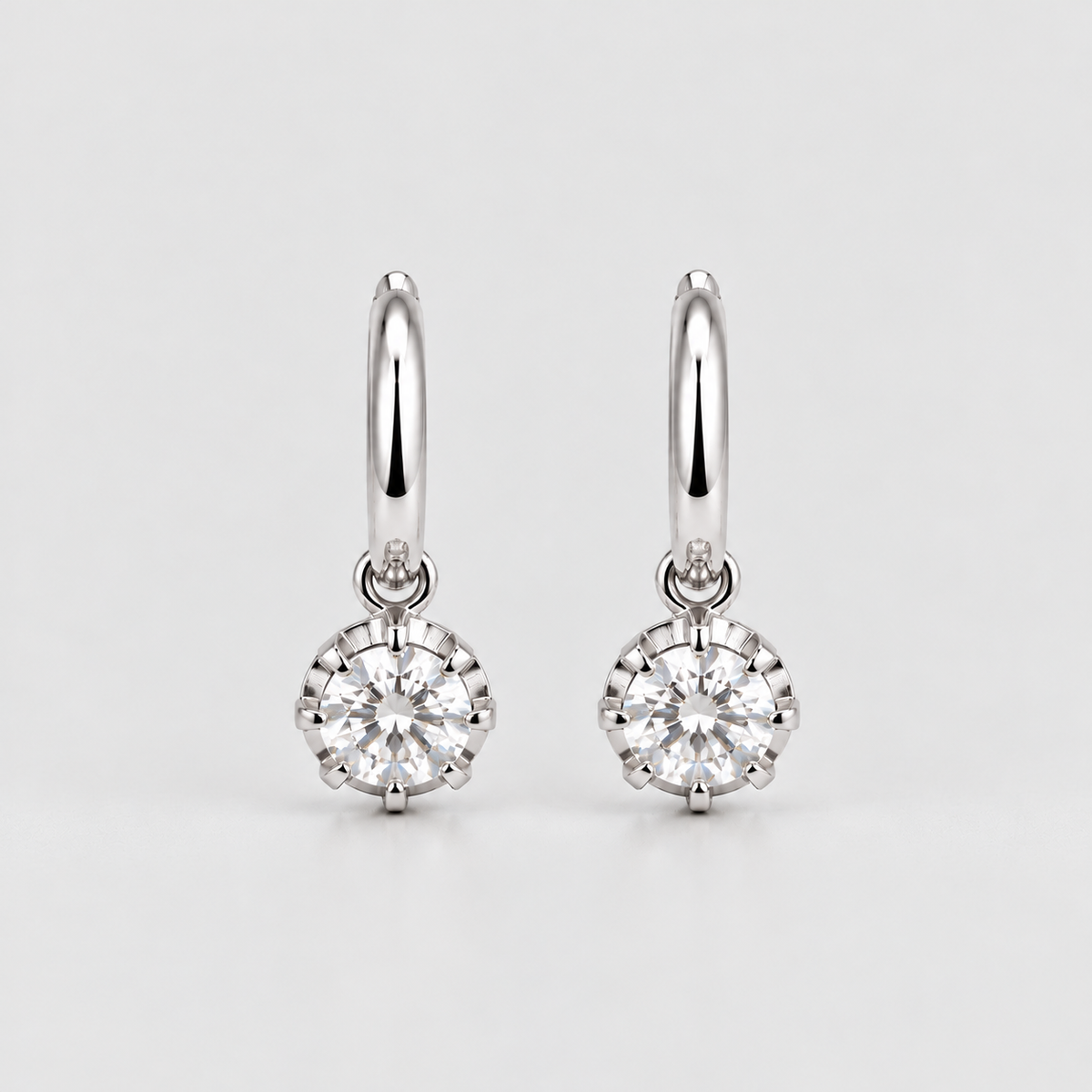 A pair of silver hoop earrings with round-cut clear gemstones in a prong setting, displayed on a light gray background.