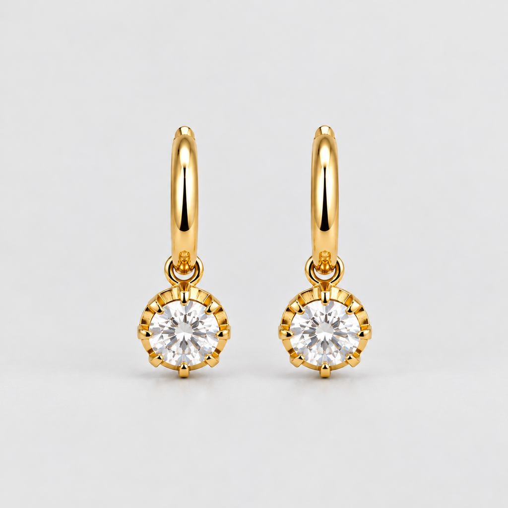 A pair of gold huggie hoop earrings with round bezel-set clear gemstones, displayed on a clean light gray background.