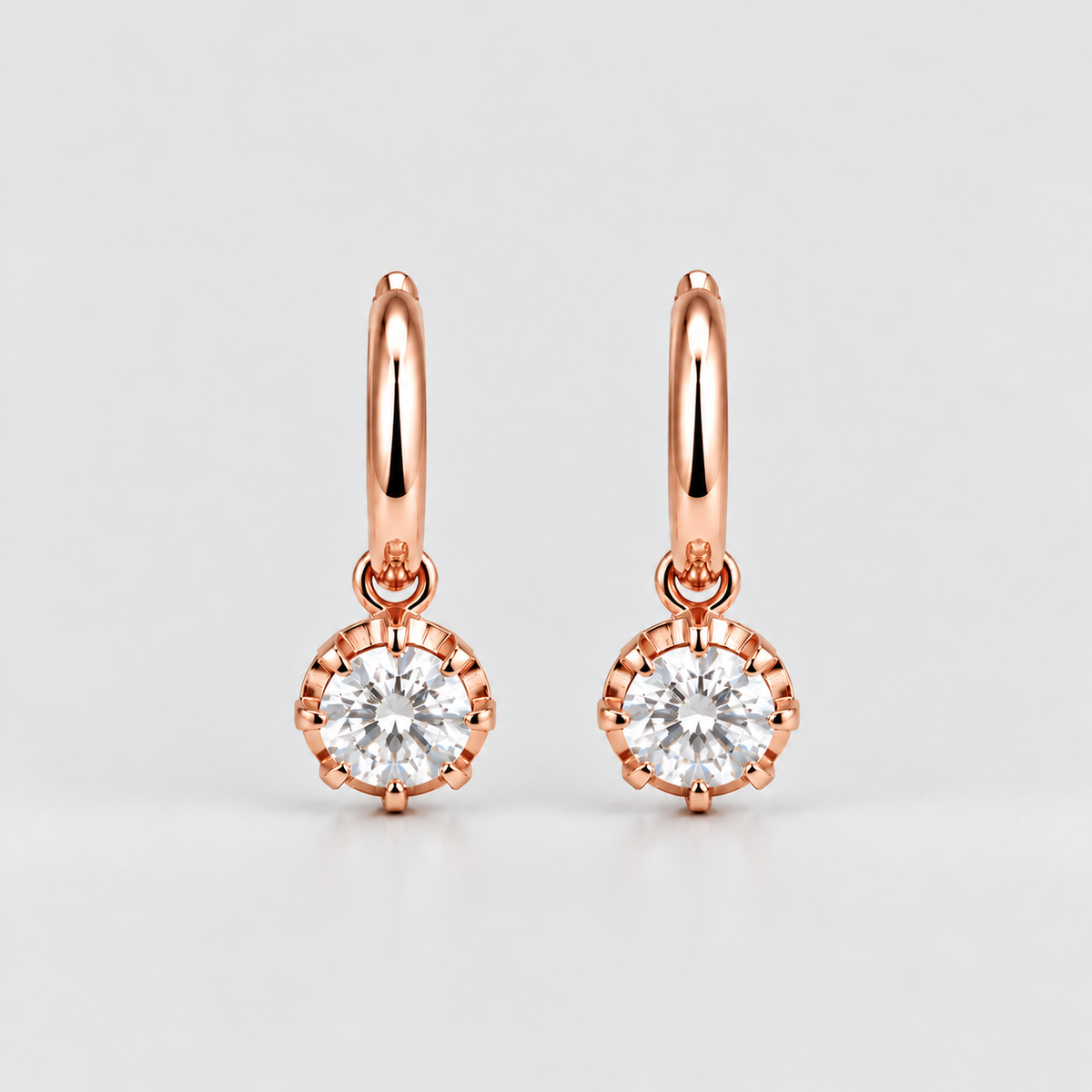 A pair of rose gold hoop earrings with round bezel-set clear gemstones, displayed on a clean light gray background.