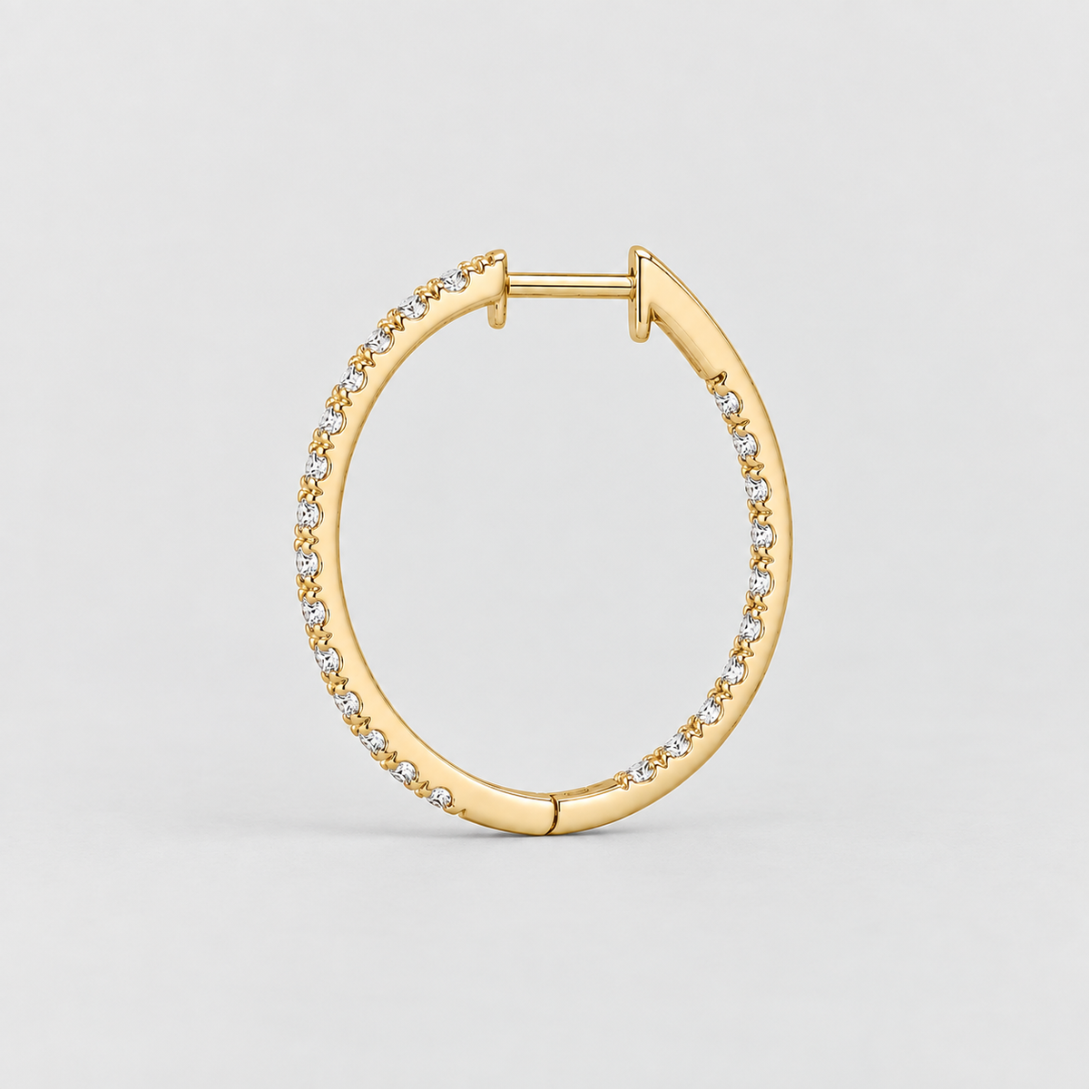 A gold hoop earring with a row of small clear stones along the front, photographed on a clean light gray background.