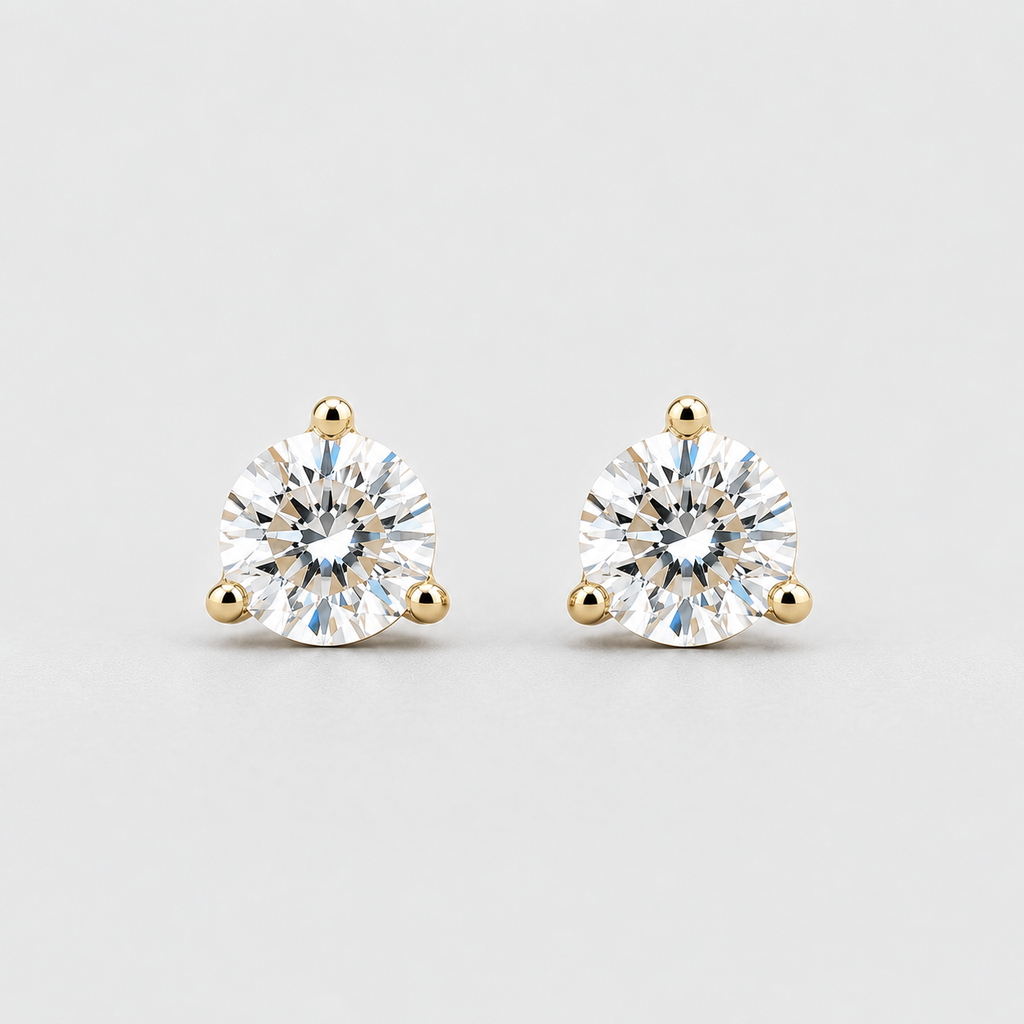 A pair of round-cut diamond stud earrings in yellow gold three-prong settings, shown on a light gray background.