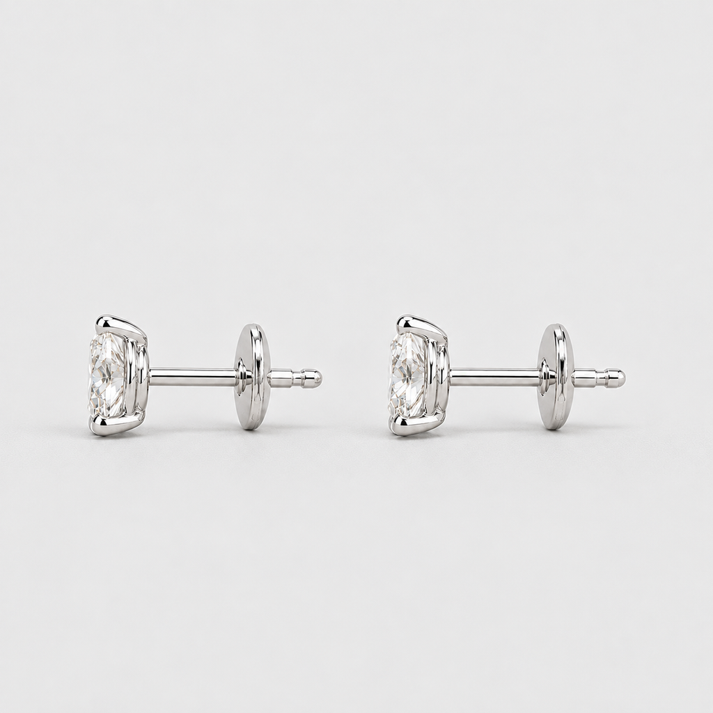 A pair of silver stud earrings with round-cut clear gemstones, shown from a side profile view on a light gray background.