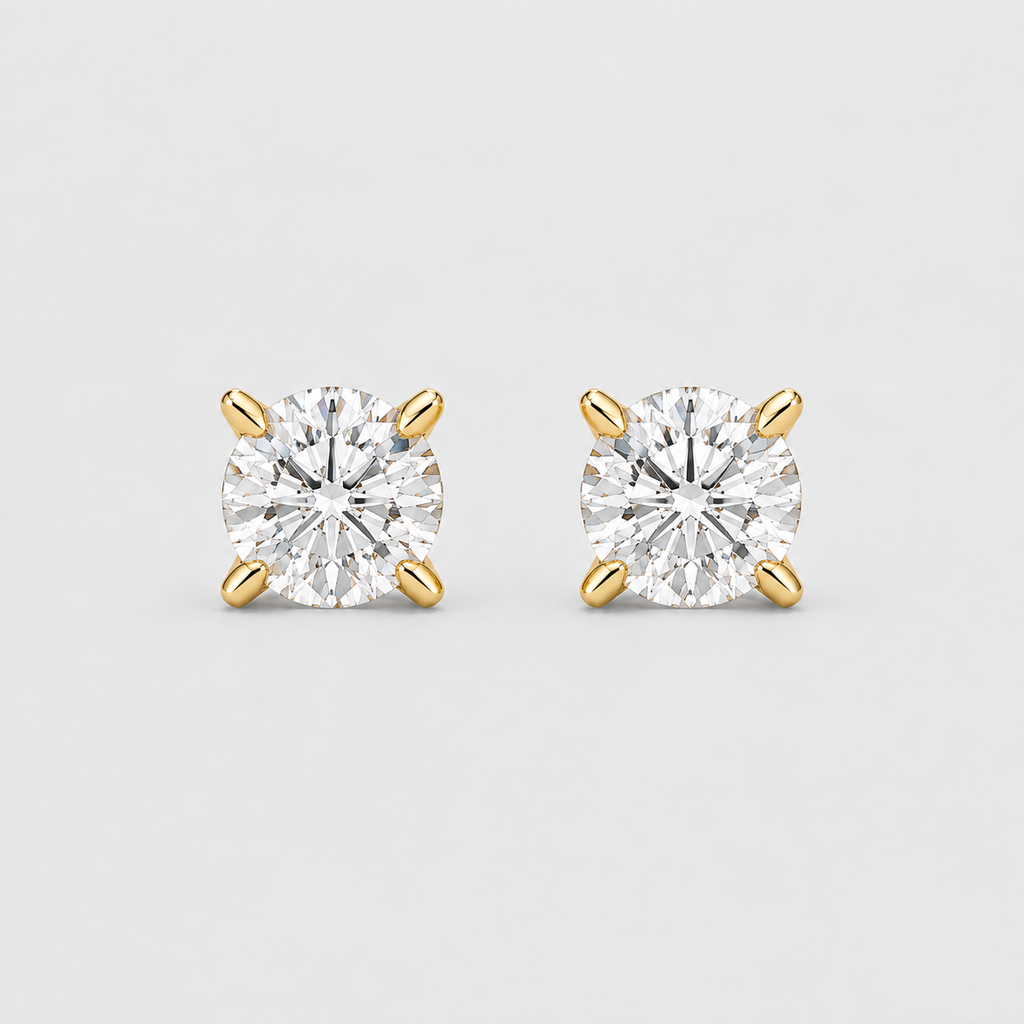 A pair of yellow gold stud earrings, each featuring a round brilliant-cut diamond set in a four-prong setting, shown on a light gray background.