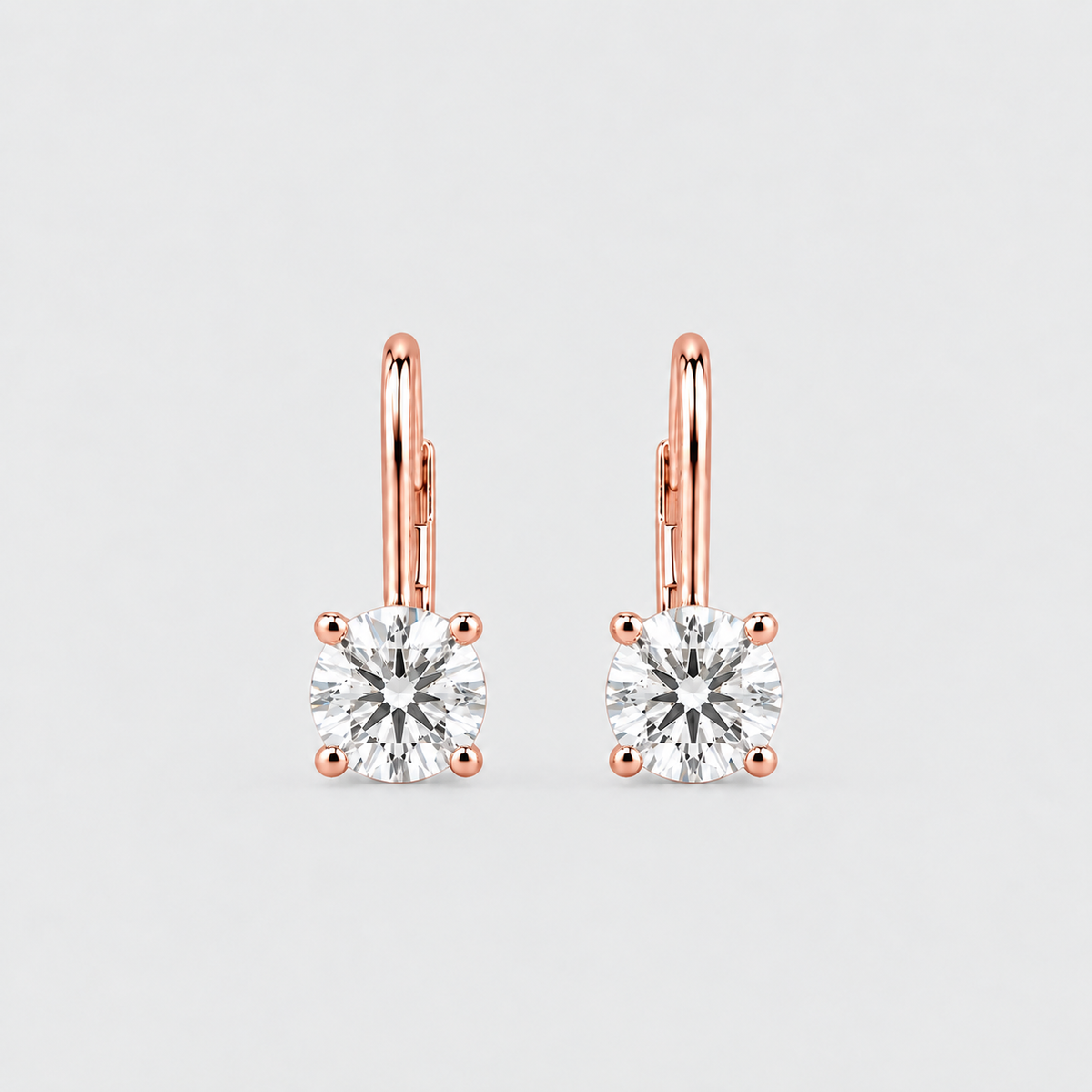 A pair of rose gold leverback earrings with square-cut clear gemstones in four-prong settings, shown on a light gray background.