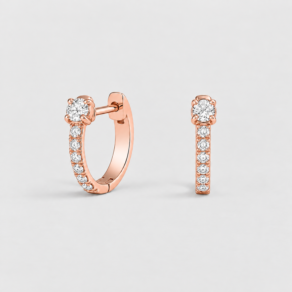 A pair of rose gold huggie hoop earrings with pavé-set clear stones, shown on a light gray background.