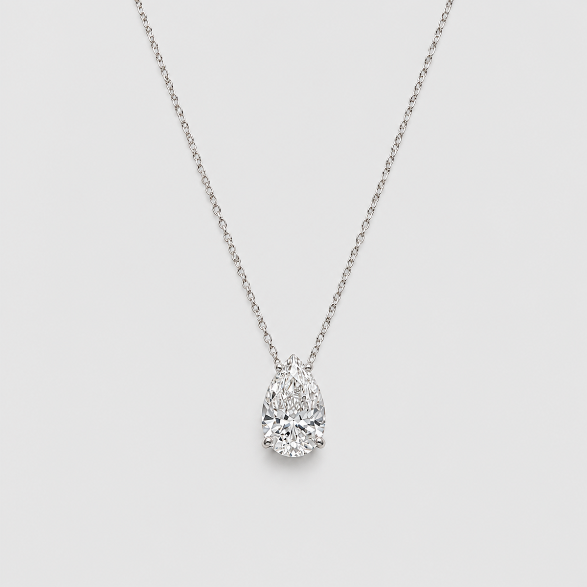 A pear-cut diamond pendant necklace on a delicate silver chain, set against a solid light gray background.