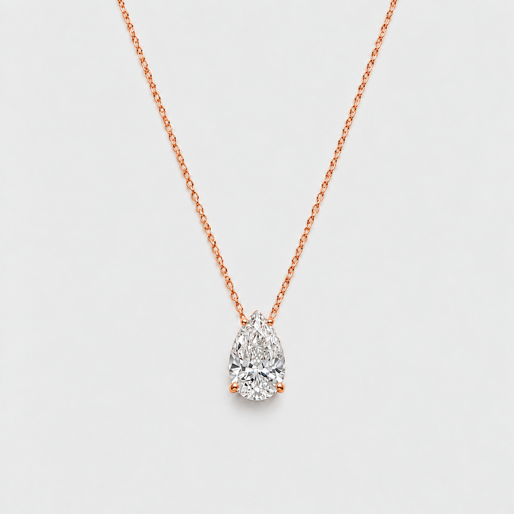 A pear-cut diamond pendant necklace in rose gold on a delicate chain, set against a clean, light gray background.