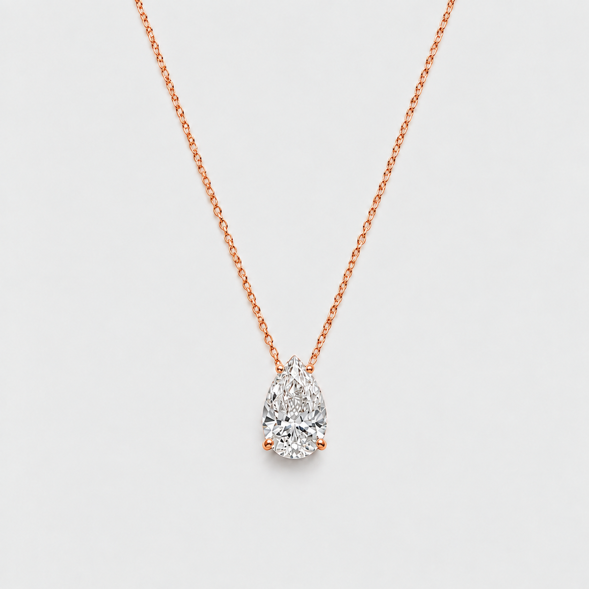 A pear-cut diamond pendant necklace in rose gold on a delicate chain, set against a clean, light gray background.