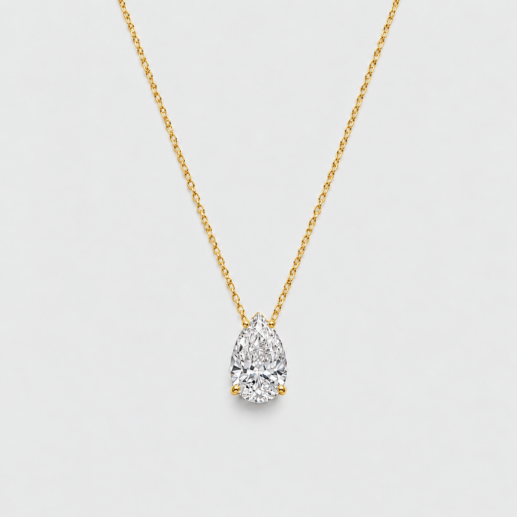 A pear-cut diamond pendant necklace on a delicate yellow gold chain, presented against a clean, light gray background.