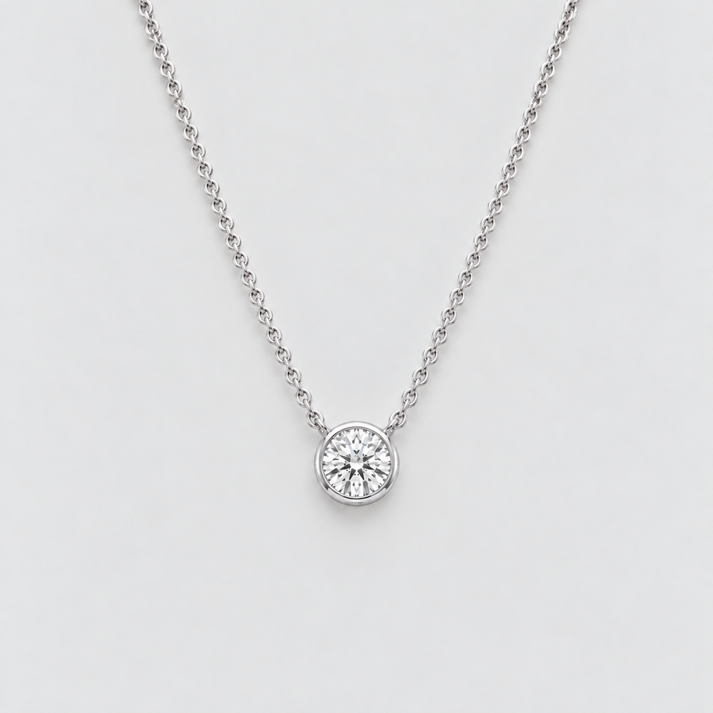 A delicate silver chain necklace with a single round bezel-set diamond pendant, shown against a clean light gray background.