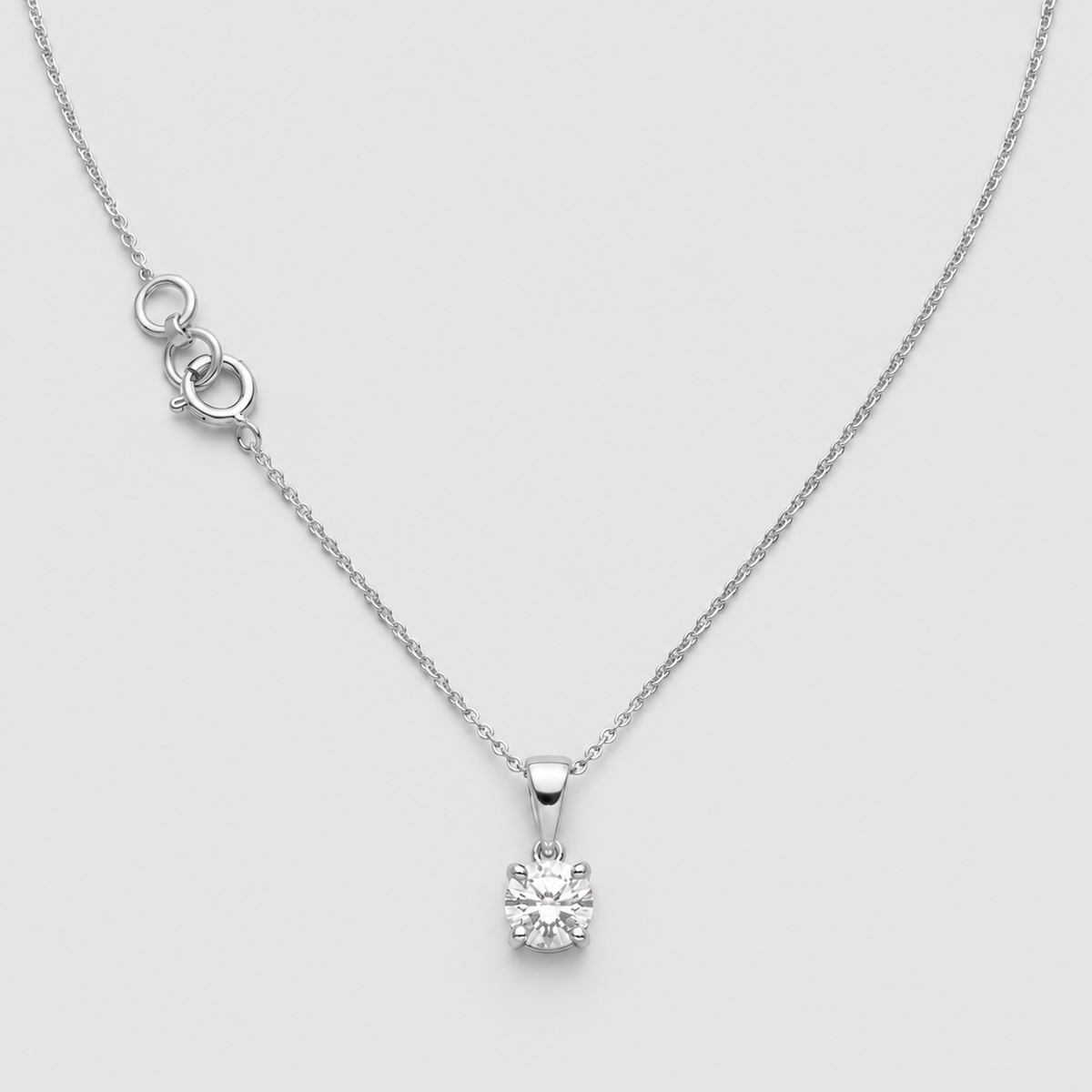 A delicate silver necklace with a single solitaire diamond pendant, displayed on a light gray background.