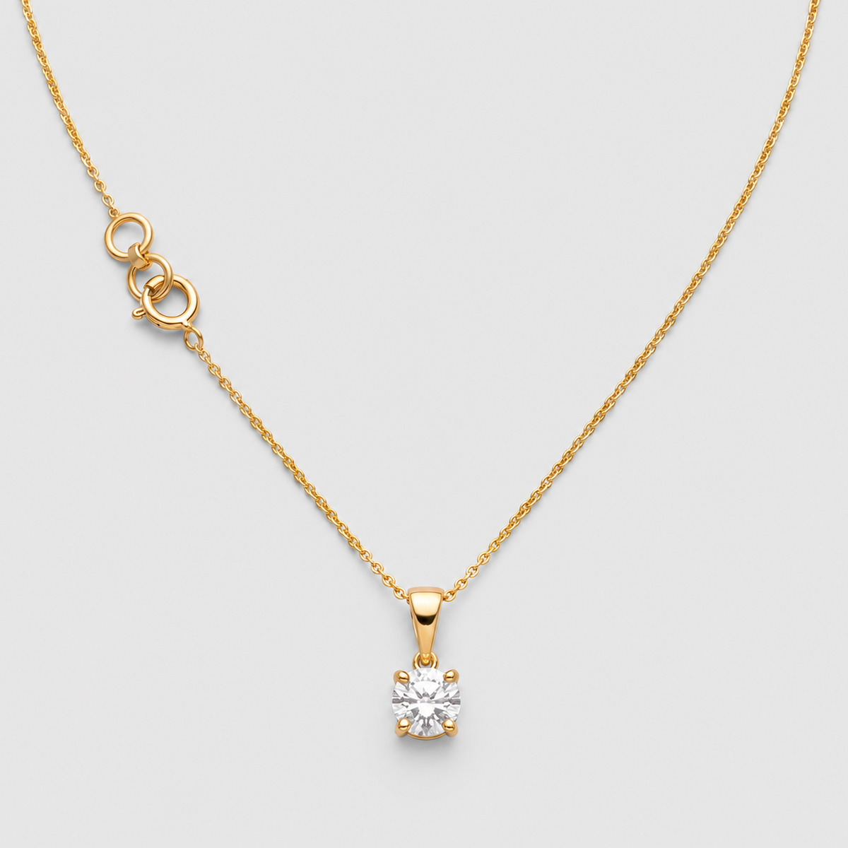 A gold necklace with a delicate chain, a small gold extender clasp, and a single solitaire diamond pendant on a light gray background.