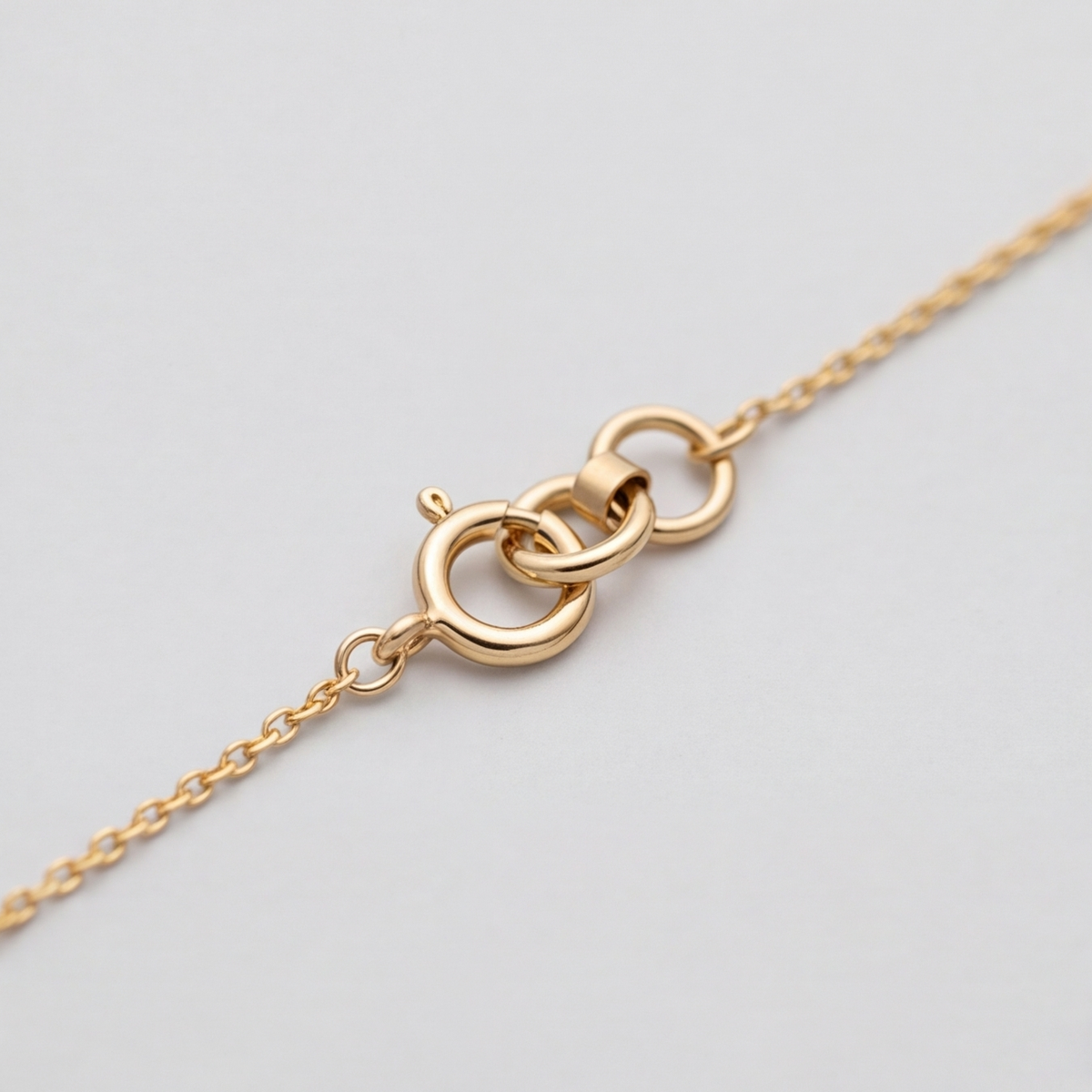 Close-up of a gold chain necklace showing a lobster clasp and interlocking ring closure on a light gray background.