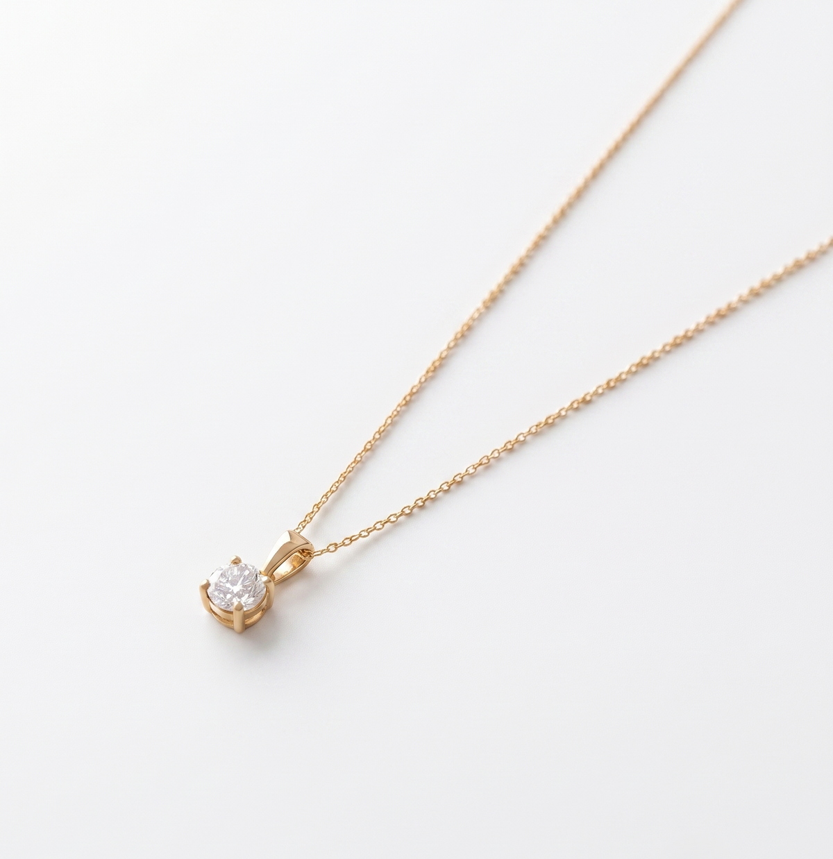 A delicate yellow gold necklace with a single-pronged pendant featuring a round brilliant-cut clear gemstone, displayed on a clean white background.