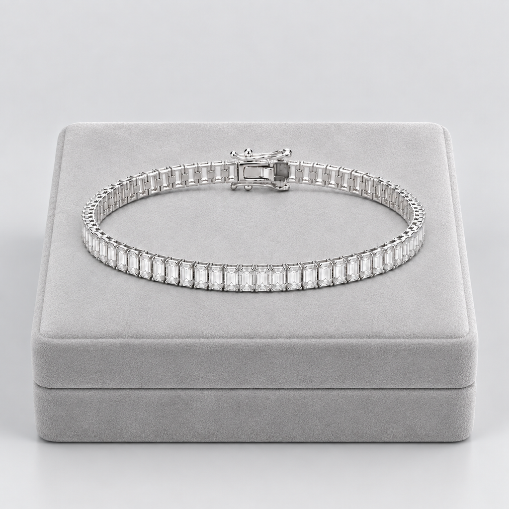 A silver tennis bracelet with baguette-cut clear stones, displayed on a light gray velvet jewelry box against a neutral gray background.
