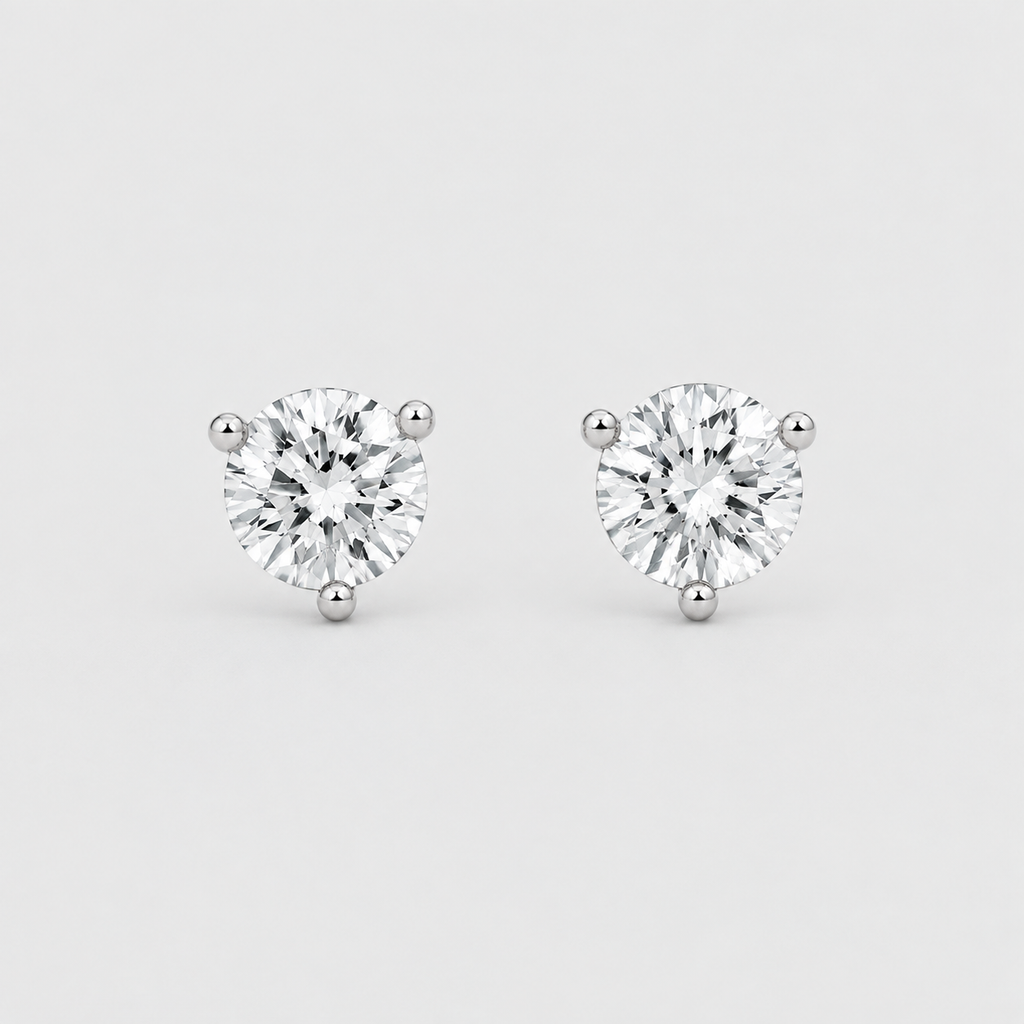 A pair of round-cut diamond stud earrings in a three-prong setting, shown on a light gray background.