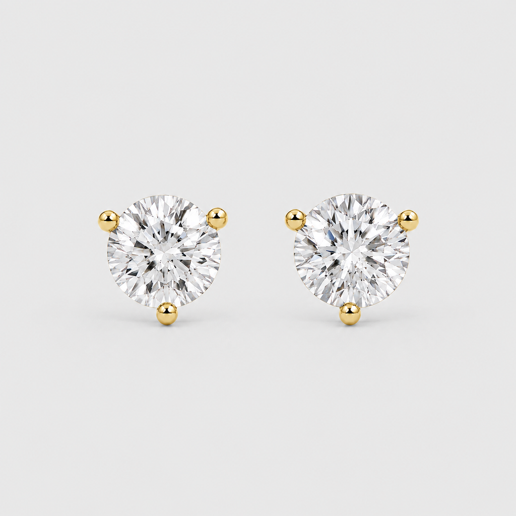 A pair of round-cut diamond stud earrings in yellow gold three-prong settings, shown on a light gray background.