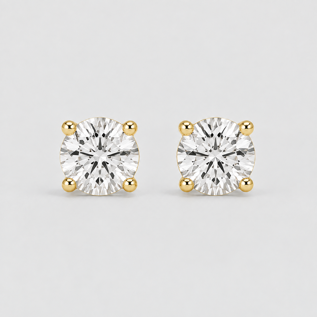 A pair of round-cut diamond stud earrings in yellow gold four-prong settings, shown on a light gray background.