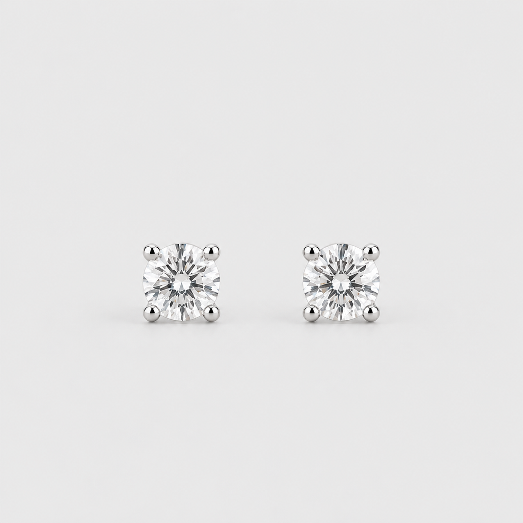 A pair of classic solitaire stud earrings featuring round brilliant-cut diamonds in four-prong settings, displayed on a clean, light gray background.