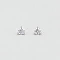 A pair of solitaire stud earrings with round brilliant-cut clear gemstones in a silver four-prong setting, displayed on a light gray background.