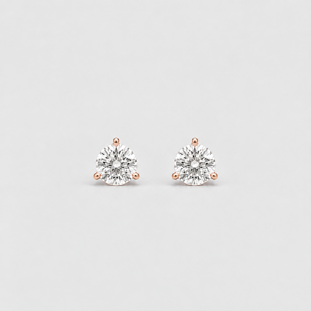 A pair of round-cut stud earrings with clear gemstones in a silver-toned setting with rose gold post accents, displayed on a light gray background.