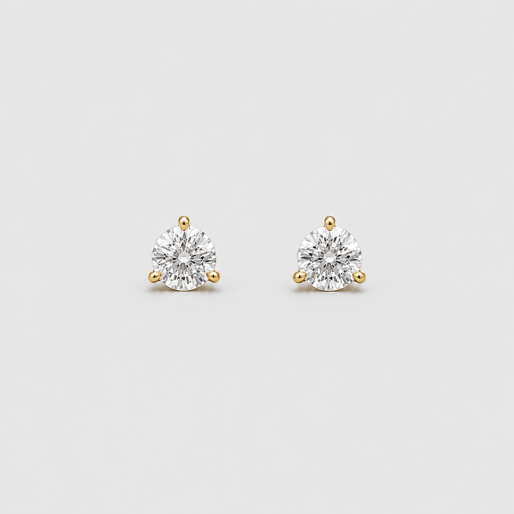 A pair of yellow gold stud earrings with round-cut clear gemstones in a three-prong setting, displayed on a light gray background.