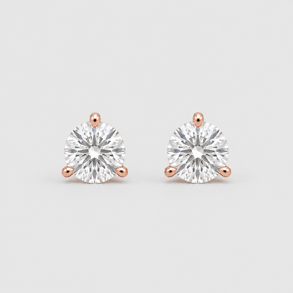 A pair of round-cut diamond stud earrings in rose gold three-prong settings, shown on a clean light gray background.