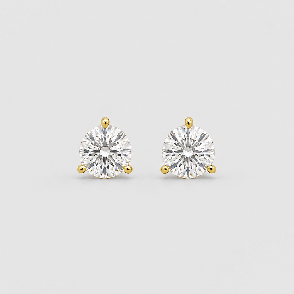 A pair of round-cut diamond stud earrings in yellow gold prong settings, shown on a light gray background.