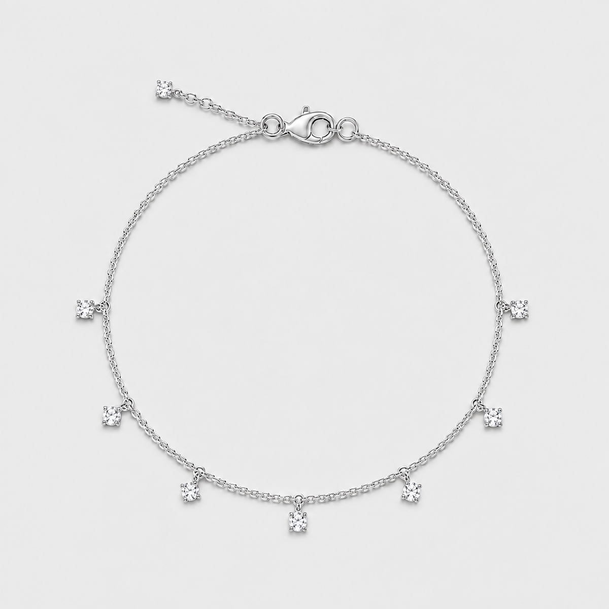 A delicate silver chain bracelet with seven small, clear, round-cut gemstone charms spaced evenly along the band, displayed on a light gray background.