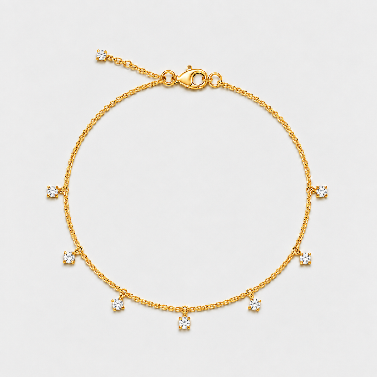 A delicate gold chain bracelet with seven small clear gemstones set in a circle, featuring a lobster clasp and extender chain, shown on a light gray background.