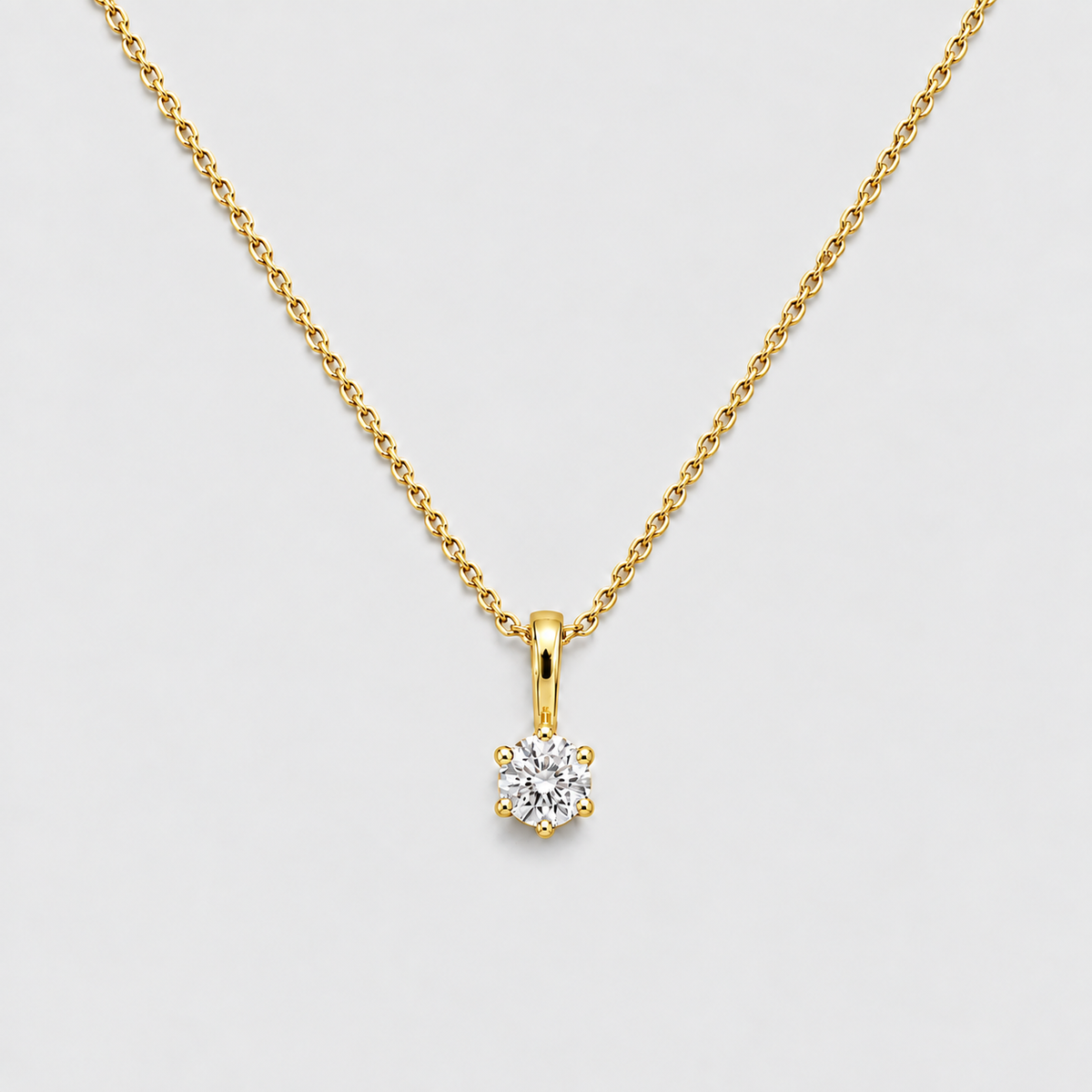A delicate yellow gold chain necklace with a small, round-cut diamond pendant set in a yellow gold bezel, displayed on a clean light gray background.