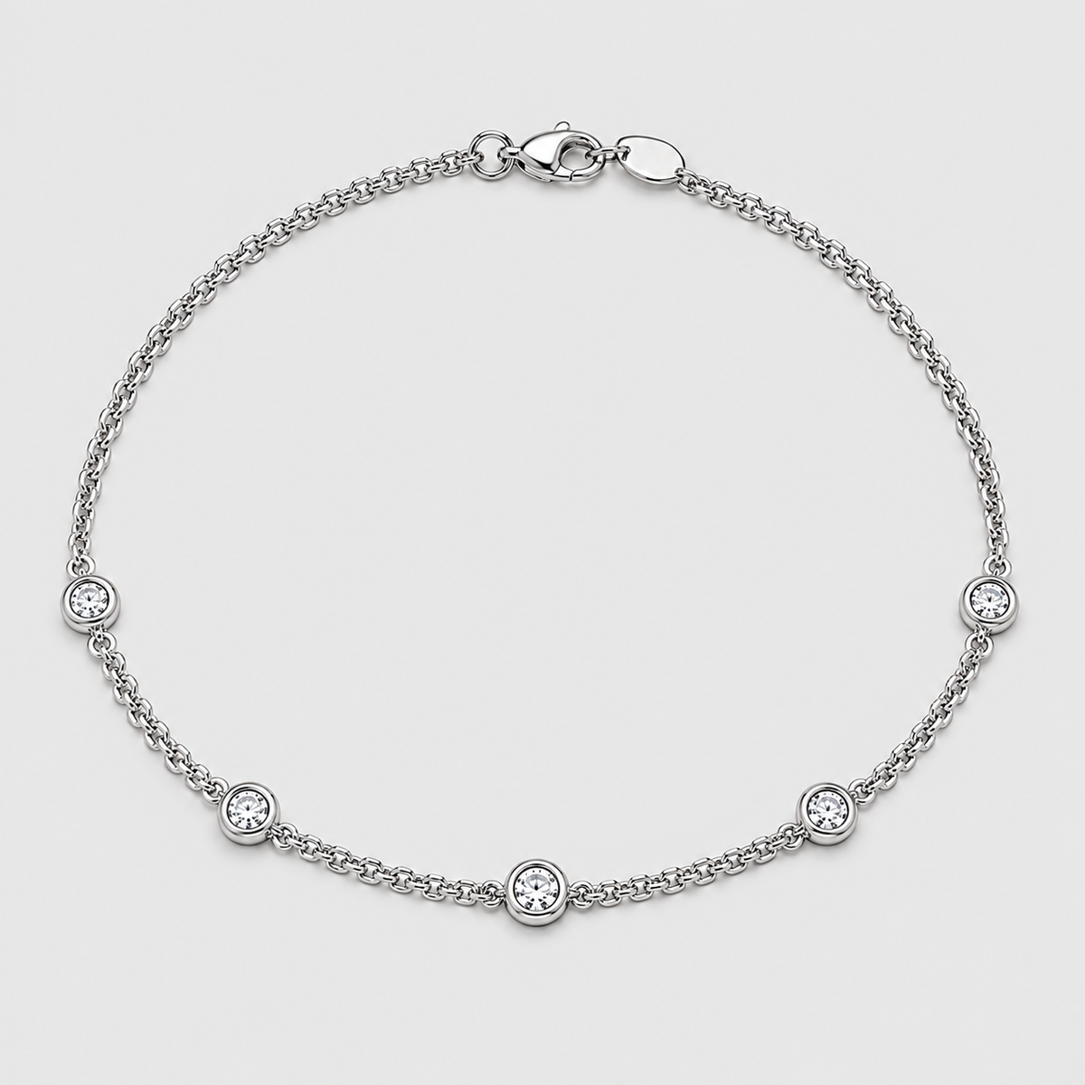 A silver chain bracelet with five small bezel-set round clear stones, displayed on a light gray background.