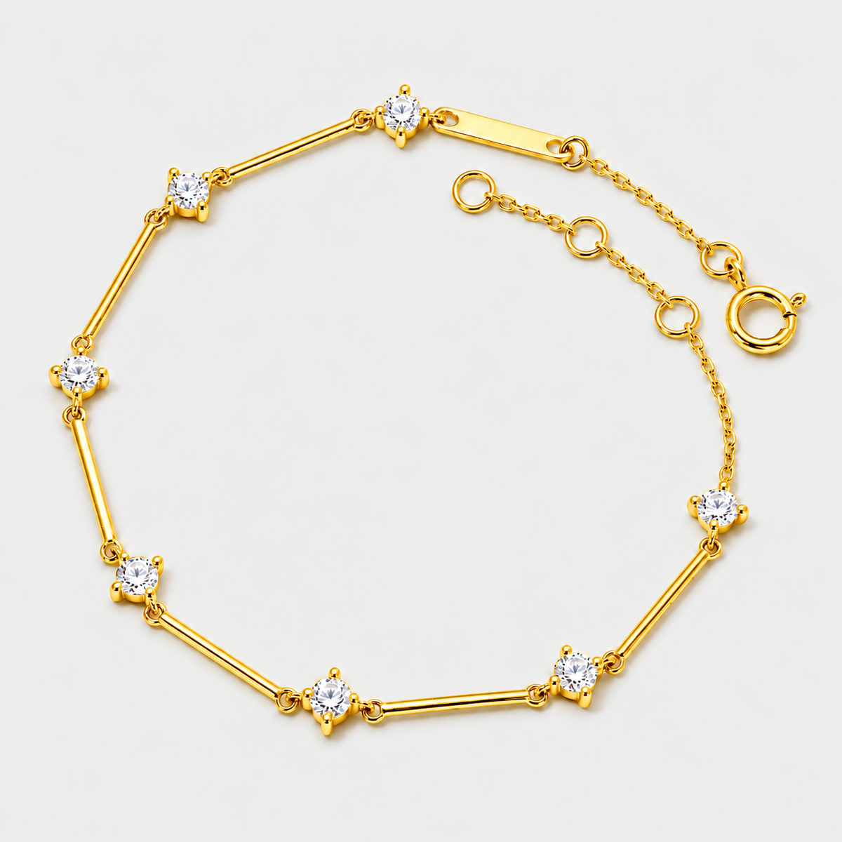 A gold bracelet with alternating round-cut clear gemstones and polished gold bars, displayed on a light gray background.