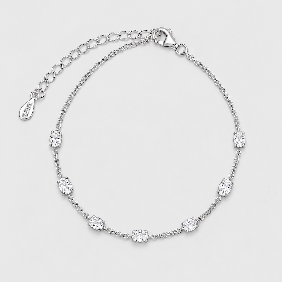 A silver chain bracelet with seven oval-cut clear stones spaced evenly along the band, featuring an adjustable lobster clasp and extension chain with a small engraved tag that reads VVD.