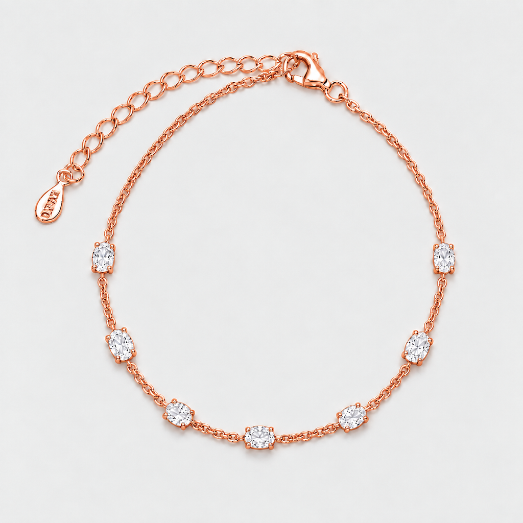 A rose gold chain bracelet with seven bezel-set clear oval gemstones, displayed on a clean light gray background.