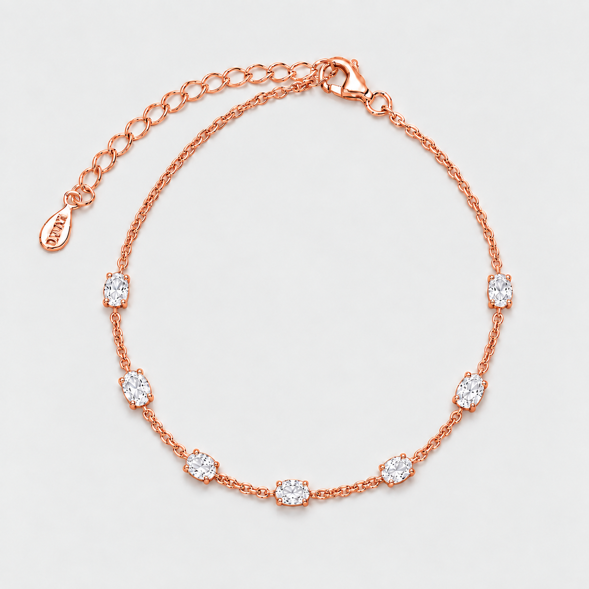 A rose gold chain bracelet with seven bezel-set clear oval gemstones, displayed on a clean light gray background.