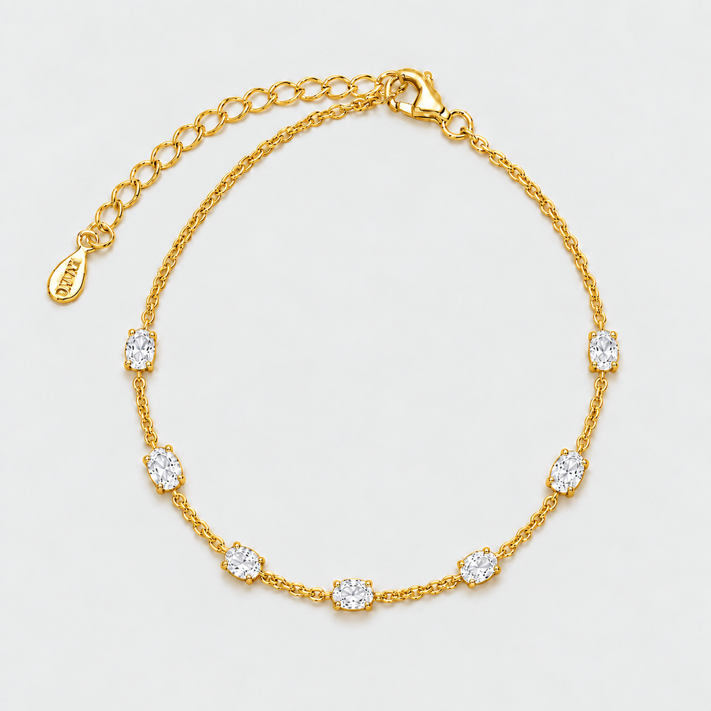 A gold chain anklet featuring seven bezel-set oval clear gemstones, displayed on a clean white background. The anklet includes an adjustable gold chain with a lobster clasp and an extension chain with a small branded tag.