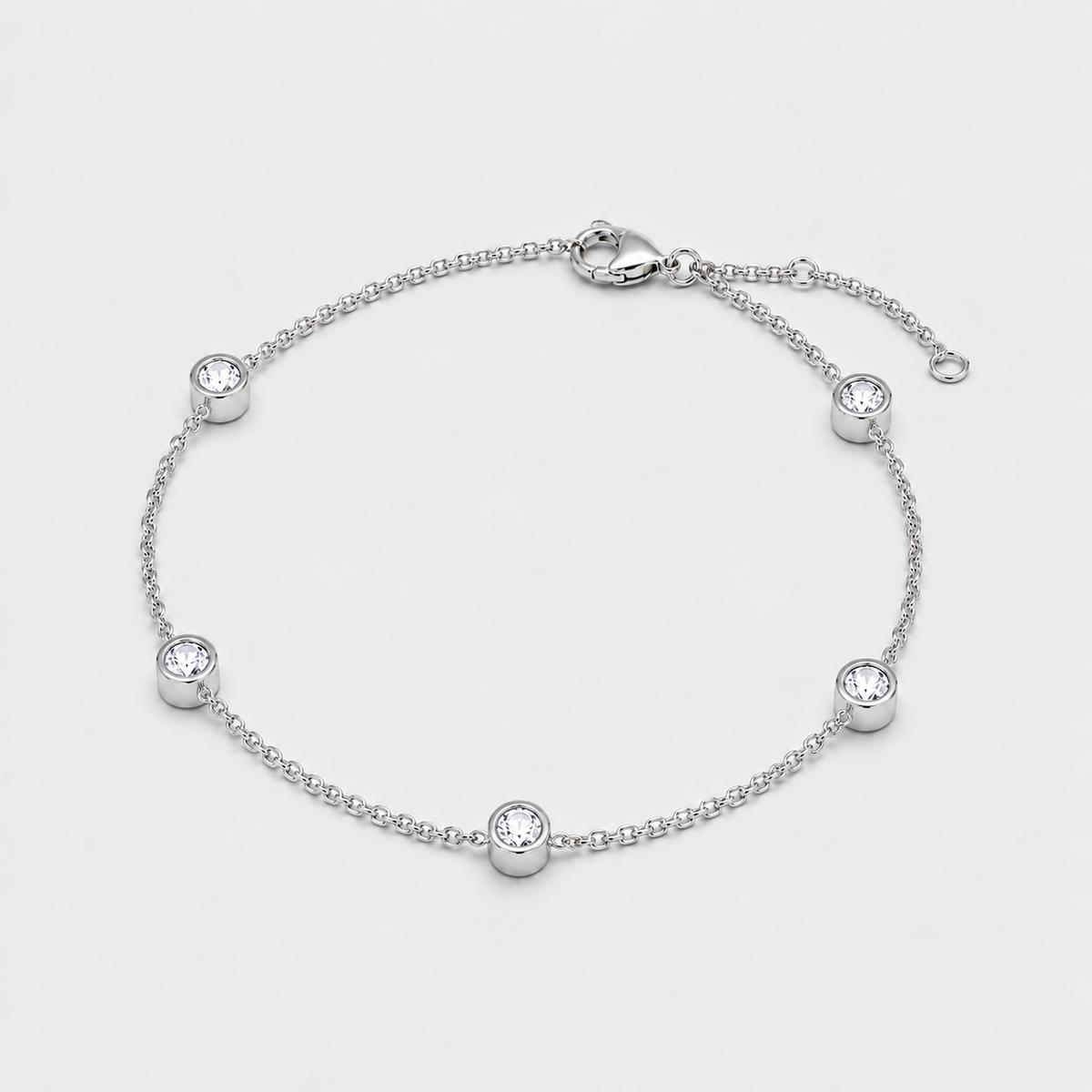 A silver chain anklet with five bezel-set clear round stones, displayed on a light gray background.
