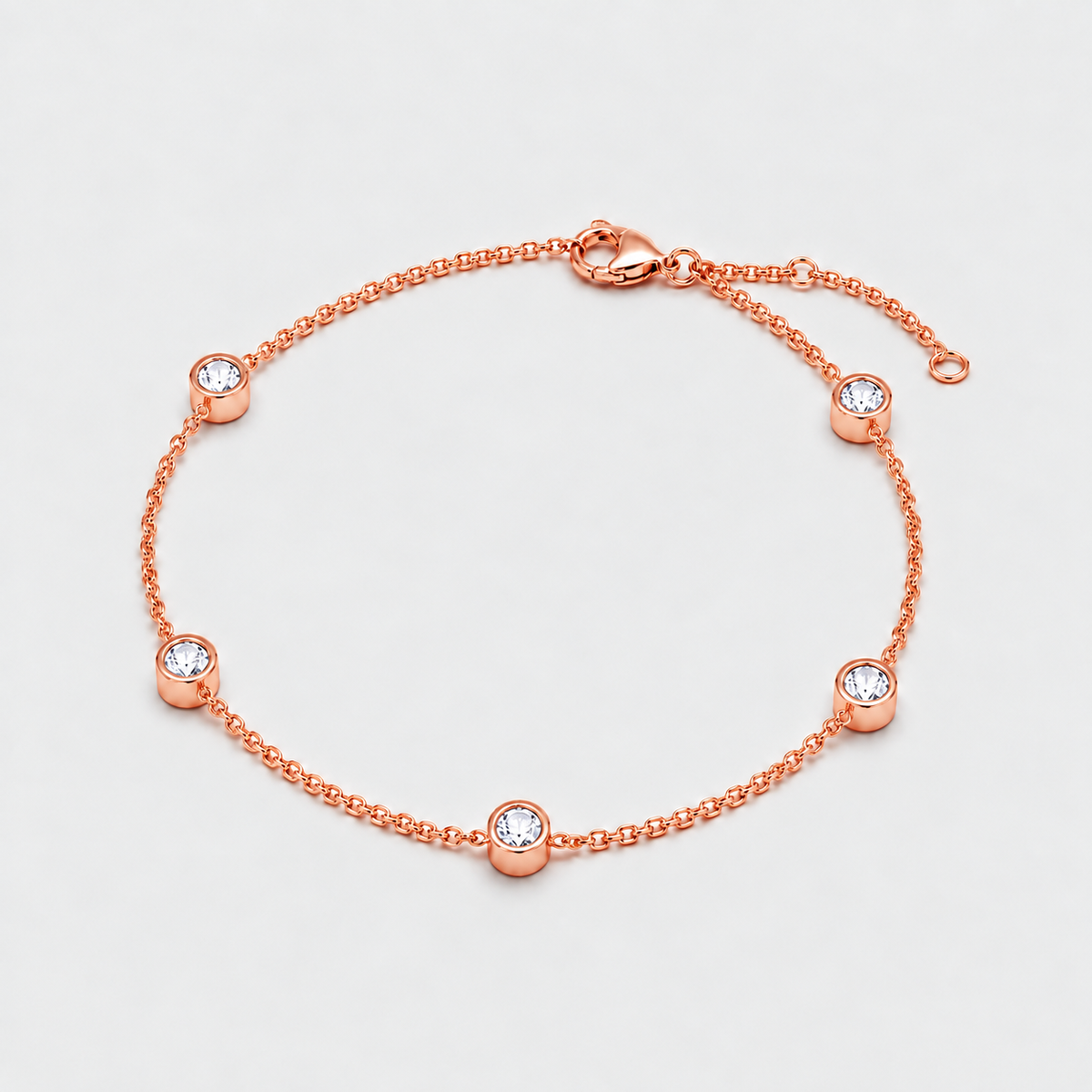 A delicate rose gold chain bracelet with five bezel-set clear round gemstones, displayed on a clean light gray background.