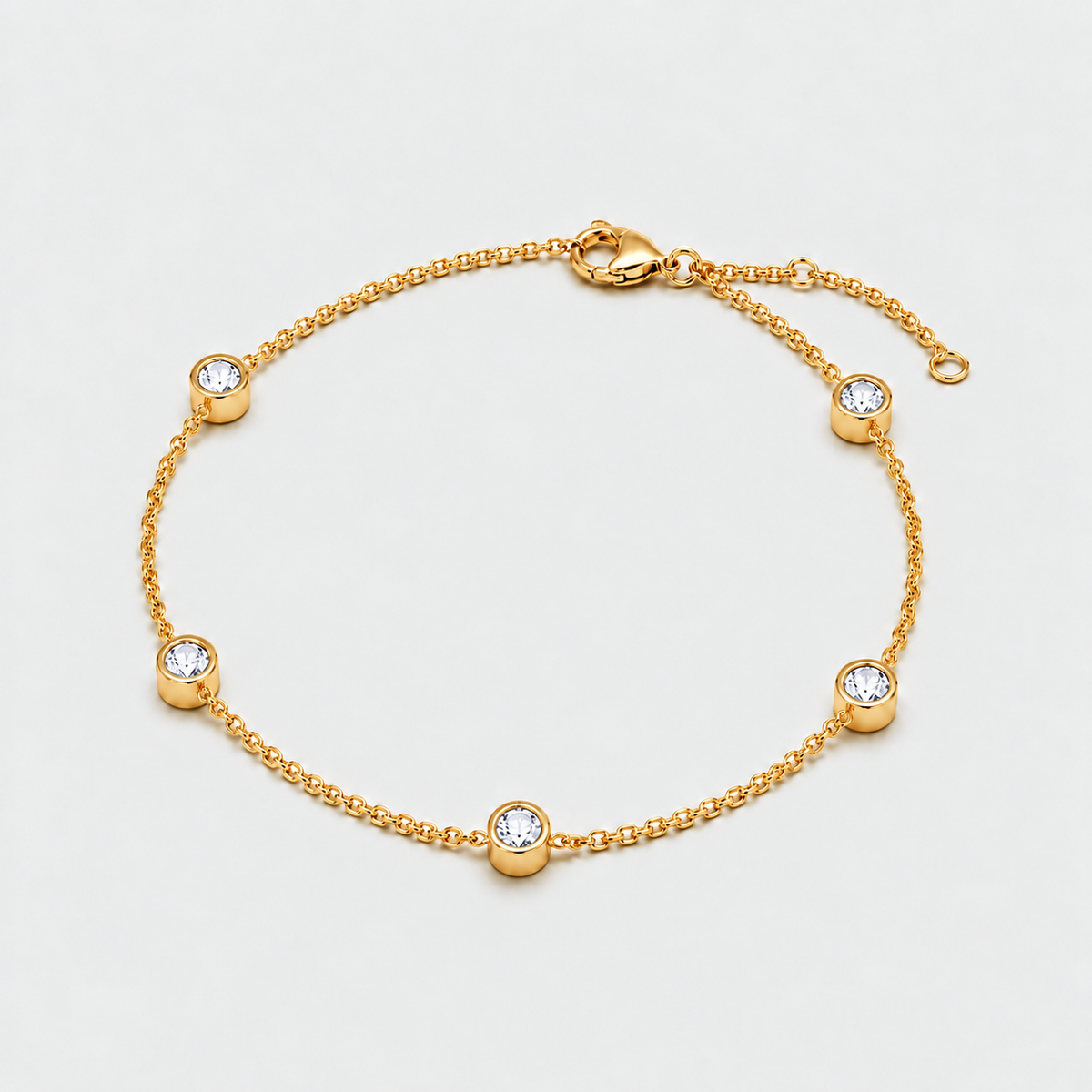 A delicate gold chain bracelet with five bezel-set round clear stones, displayed on a clean light gray background.