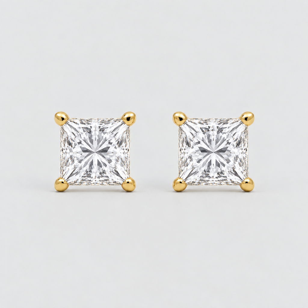 A pair of princess-cut diamond stud earrings in yellow gold four-prong settings, shown on a light gray background.