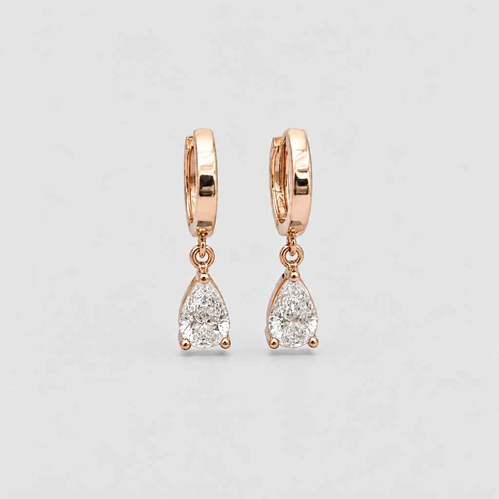 A pair of rose gold huggie hoop earrings with teardrop-shaped clear gemstones, displayed on a light gray background.