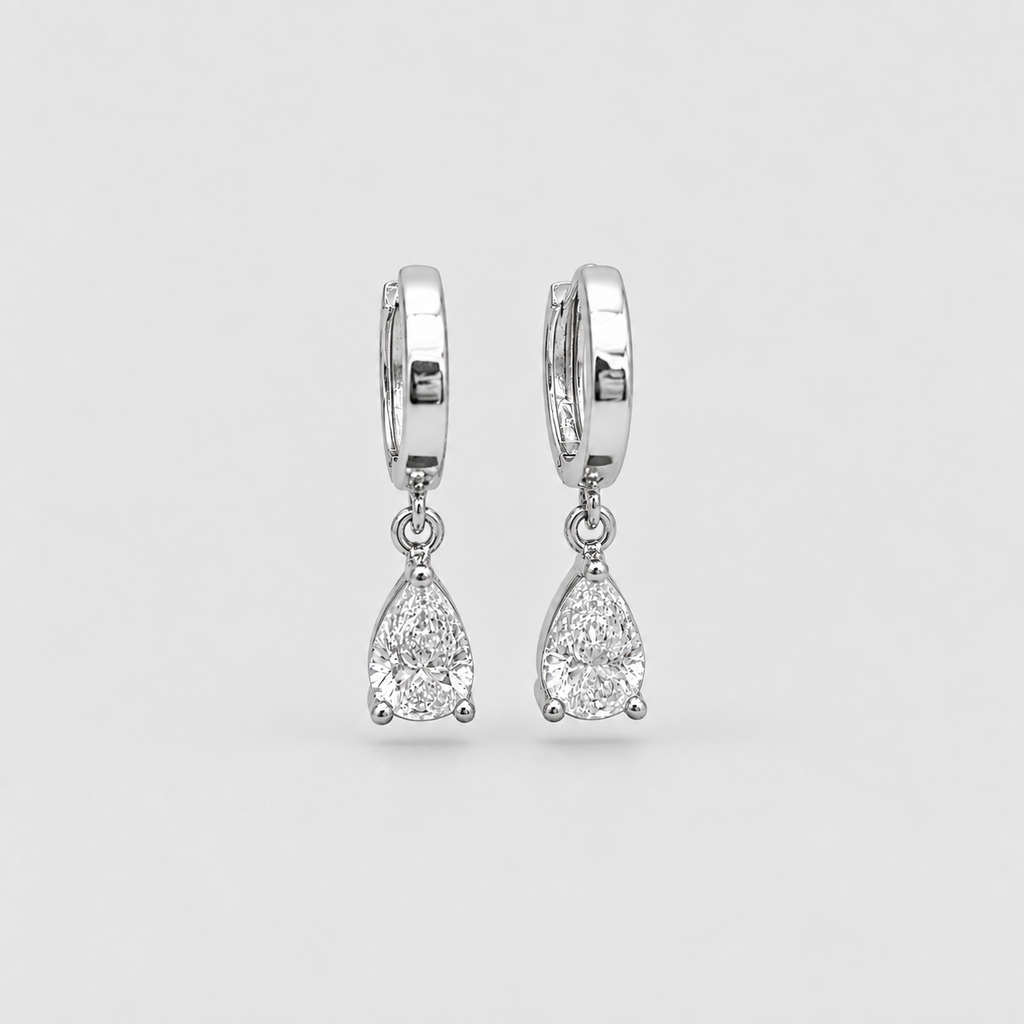 A pair of silver huggie hoop earrings with teardrop-shaped clear gemstones, shown against a light gray background.